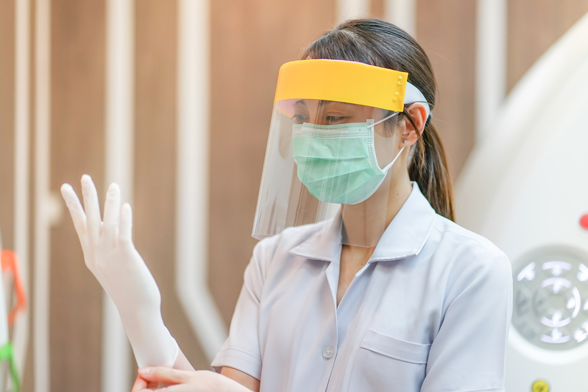 Girl with face shield, mask and gloves on in a health setting.