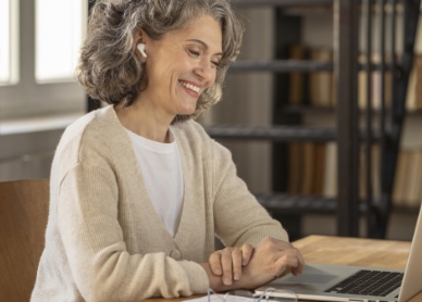 Smiling older woman sitting at a desk in front of a laptop.