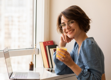 Girl holding an orange drink in a glass, sitting in front of a laptop.